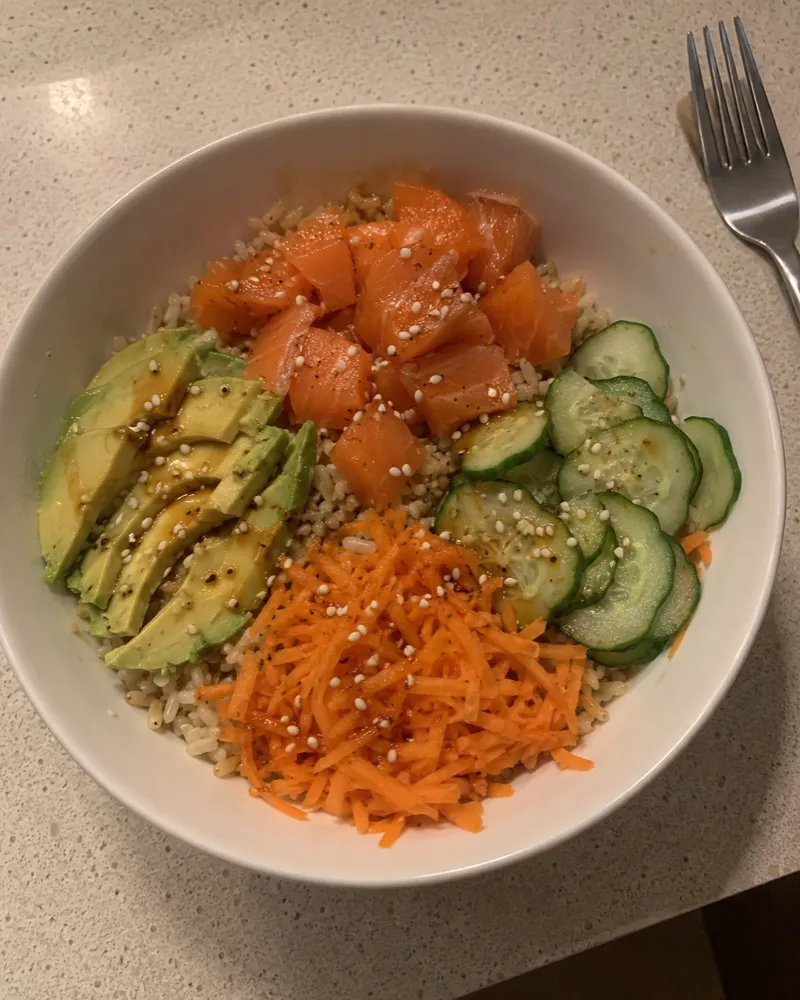 Bol de arroz integral con taquitos de salmón ahumado, aguacate, pepino, zanahoria y sésamo