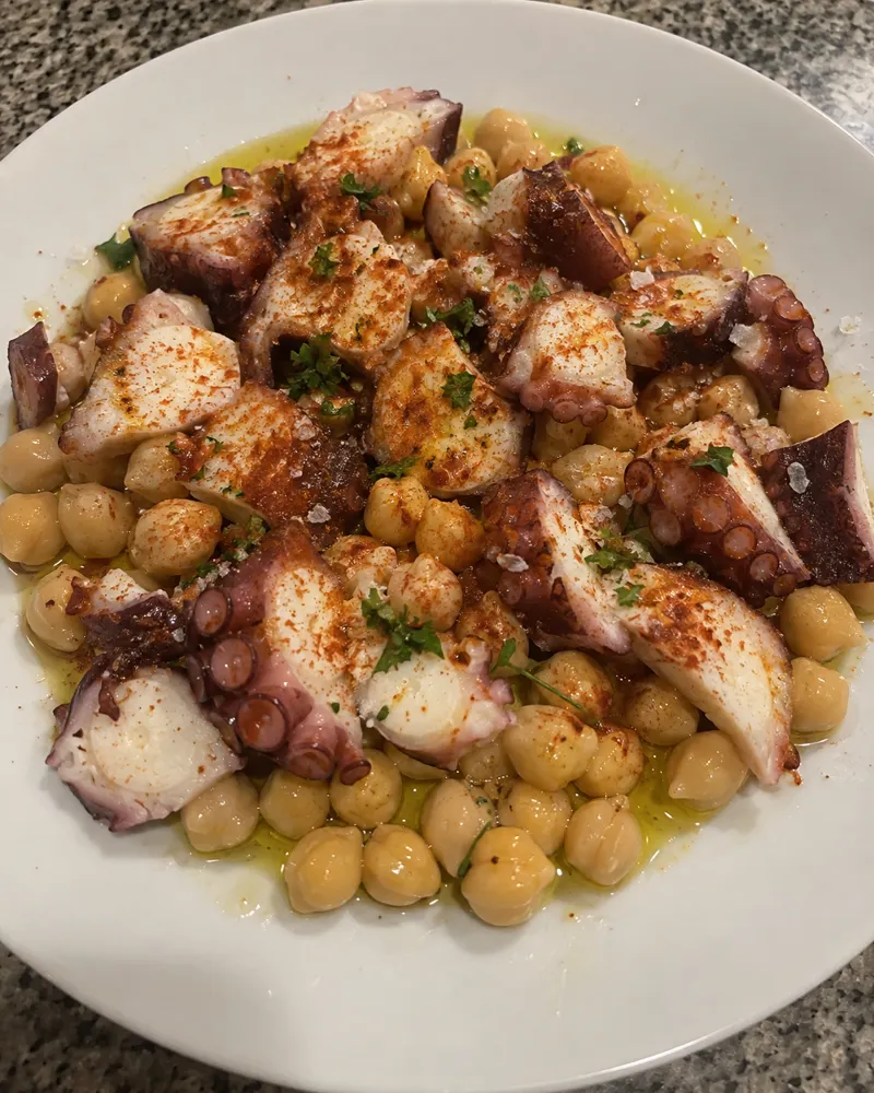 Plato de madera con garbanzos, rodajas de pulpo, pimentón y aceite de oliva
